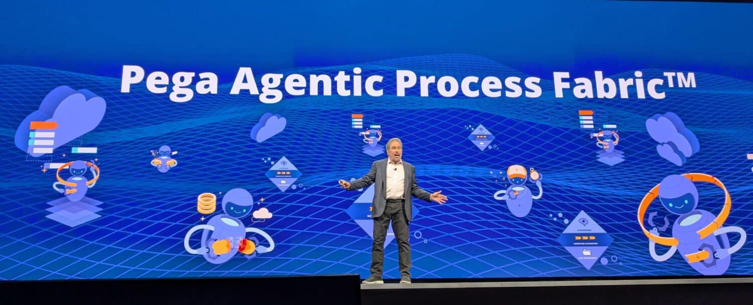 Pega_Agentic_Process_Fabric Een man in zakelijke kleding staat op het podium voor een blauw scherm met daarop "Pega Agentic Process Fabric™" en digitale afbeeldingen, die innovaties zoals Pega Blueprint benadrukken met aantrekkelijke pictogrammen.