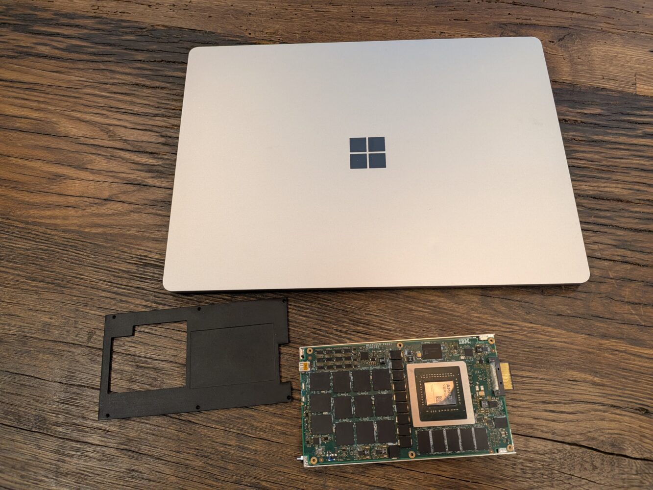 Een gesloten Microsoft Surface-laptop, een zwart plastic frame en een computerprintplaat worden op een houten oppervlak geplaatst.