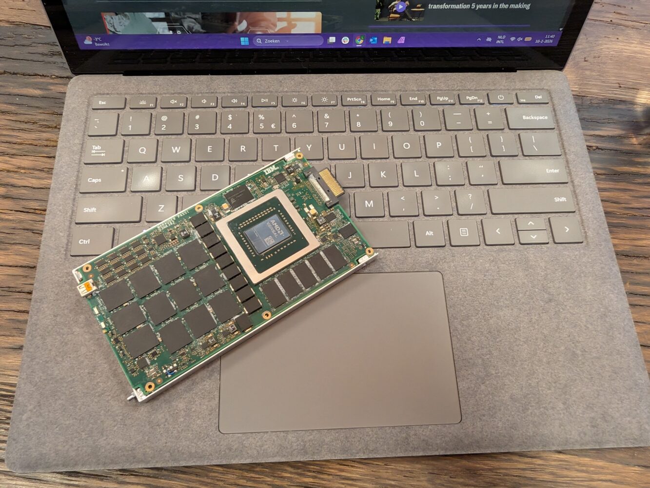 Een grafische computerkaart rust op het toetsenbord en touchpad van een open laptop die op een houten oppervlak staat.